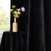 A vase of yellow and white flowers sits on a black velvet draped table next to a black curtain.