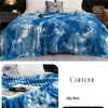 A blue and white tie-dye flannel fleece throw blanket draped over a bed.