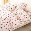 A set of three white duvet covers and pillowcases with a red heart print on a bed.