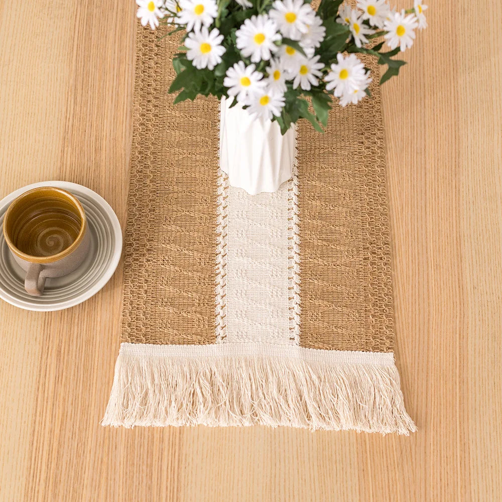 Boho linen cotton table runner with tassels placed on a wooden table next to a white cup and flowers.