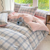 A pink and blue plaid duvet cover set with matching pillows and a pair of light blue headphones on a bed.