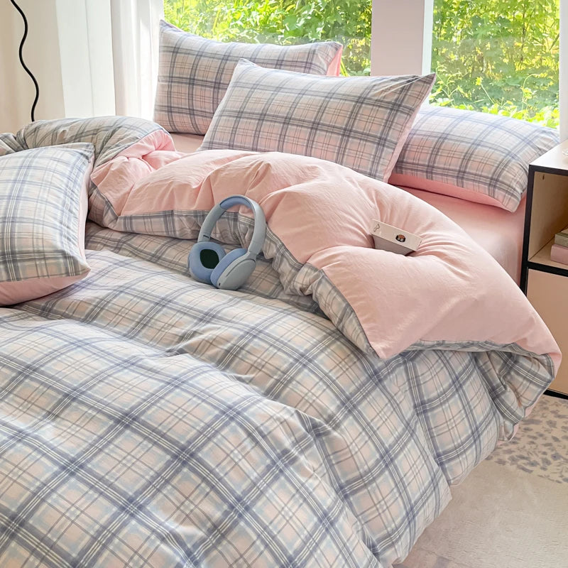 A pink and blue plaid duvet cover set with matching pillows and a pair of light blue headphones on a bed.