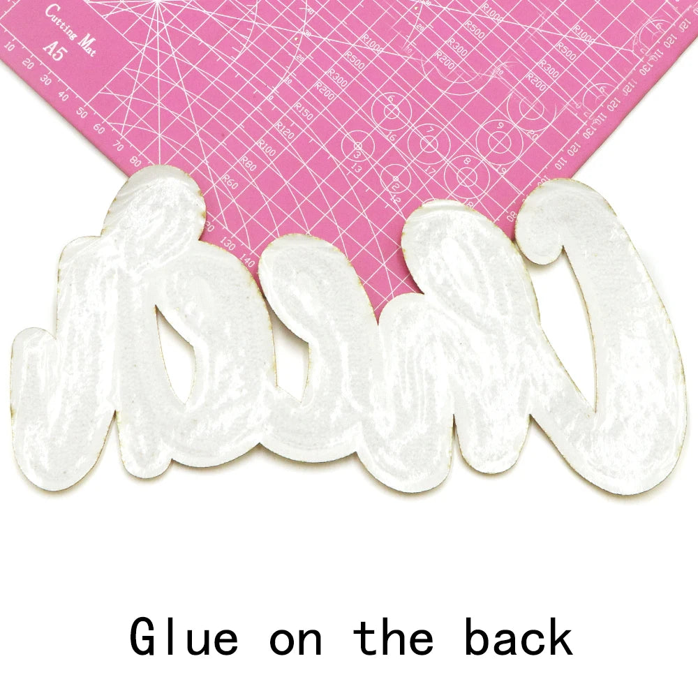 White embroidered cheer letter iron-on patch shown next to a pink ruler.
