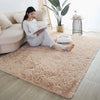 A fluffy beige rug is placed on a light wood floor next to a sofa and potted plant.