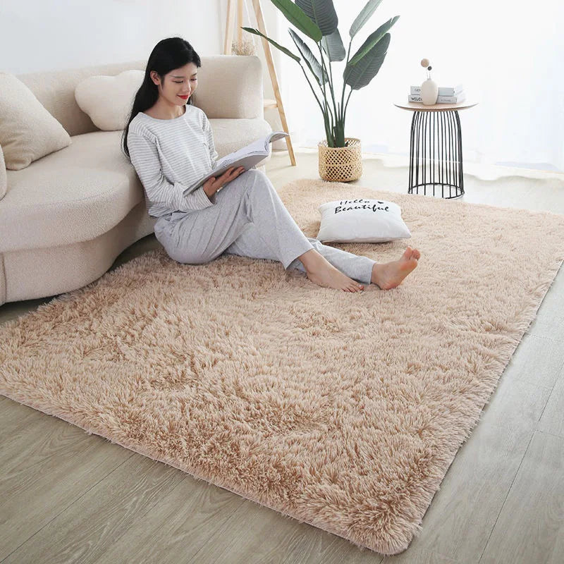 A fluffy beige rug is placed on a light wood floor next to a sofa and potted plant.