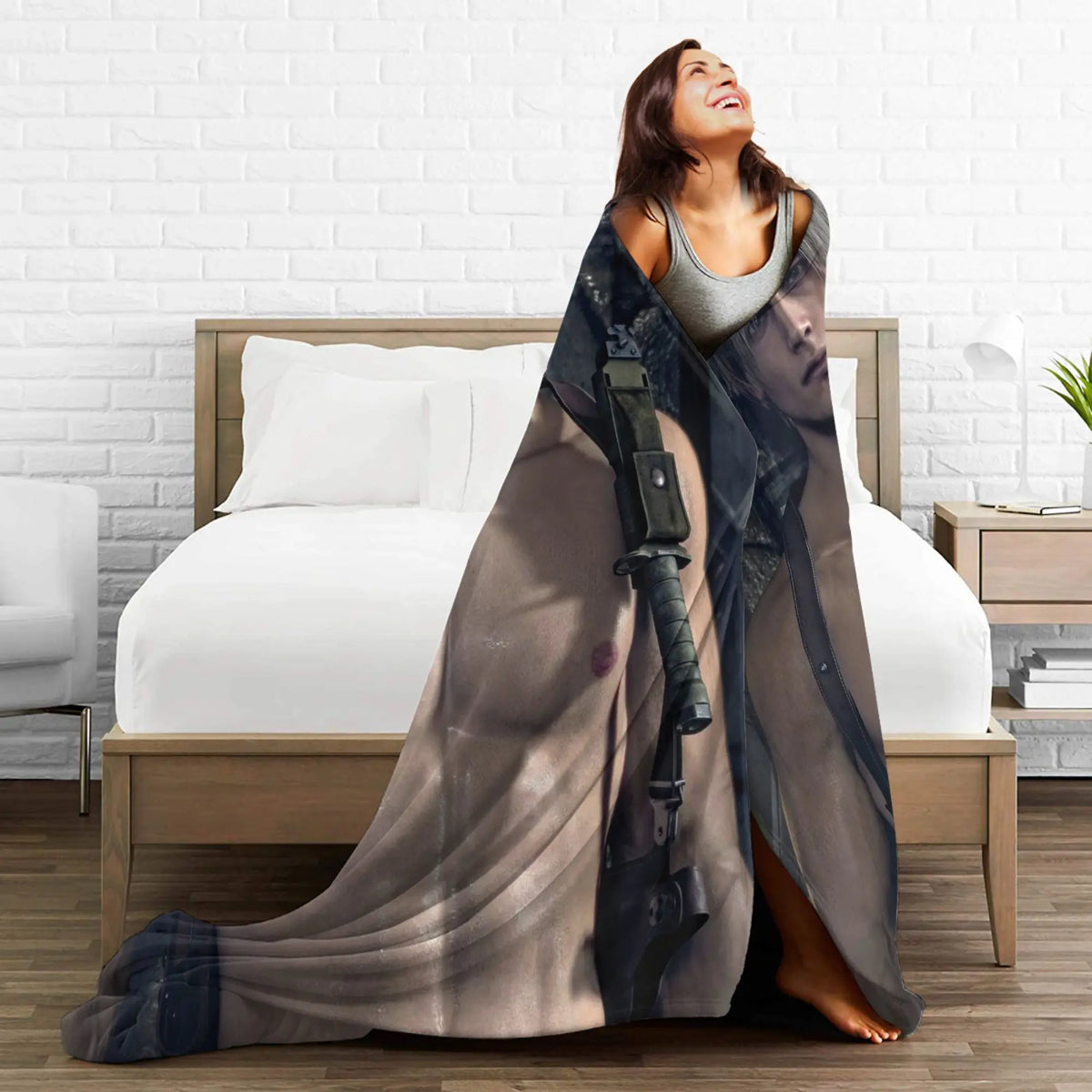 A woman is draped in a sheer, dark gray graphic throw blanket lying on a bed.