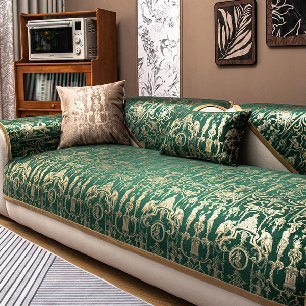 A luxury velvet sofa cover in deep green with gold damask patterns and decorative pillows.
