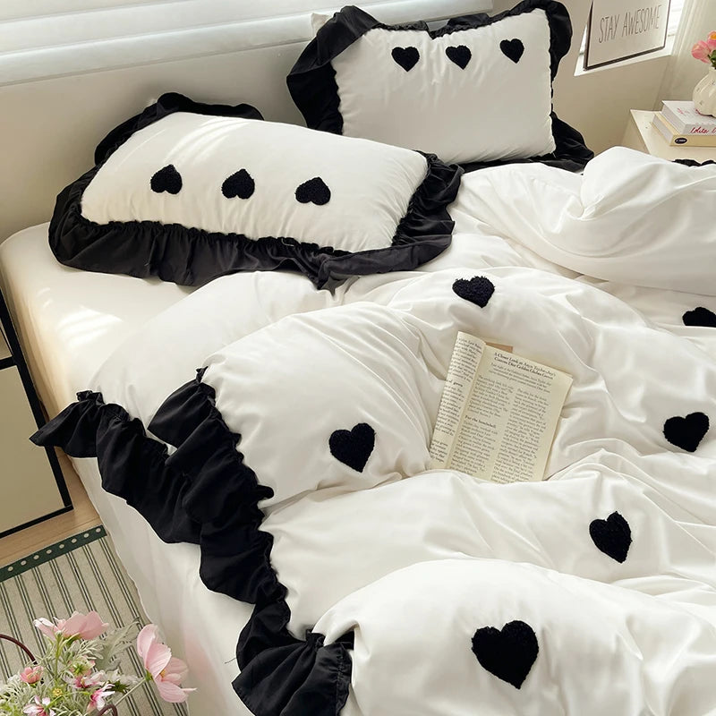 A white duvet set with black embroidered hearts and ruffled trim is displayed on a bed.