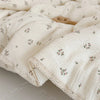 A close-up of a cream-colored muslin blanket with a delicate floral print, folded and displayed.