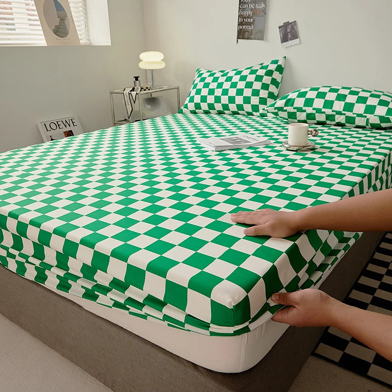 A green and white checkered fitted sheet is being placed on a bed, with a hand visible.
