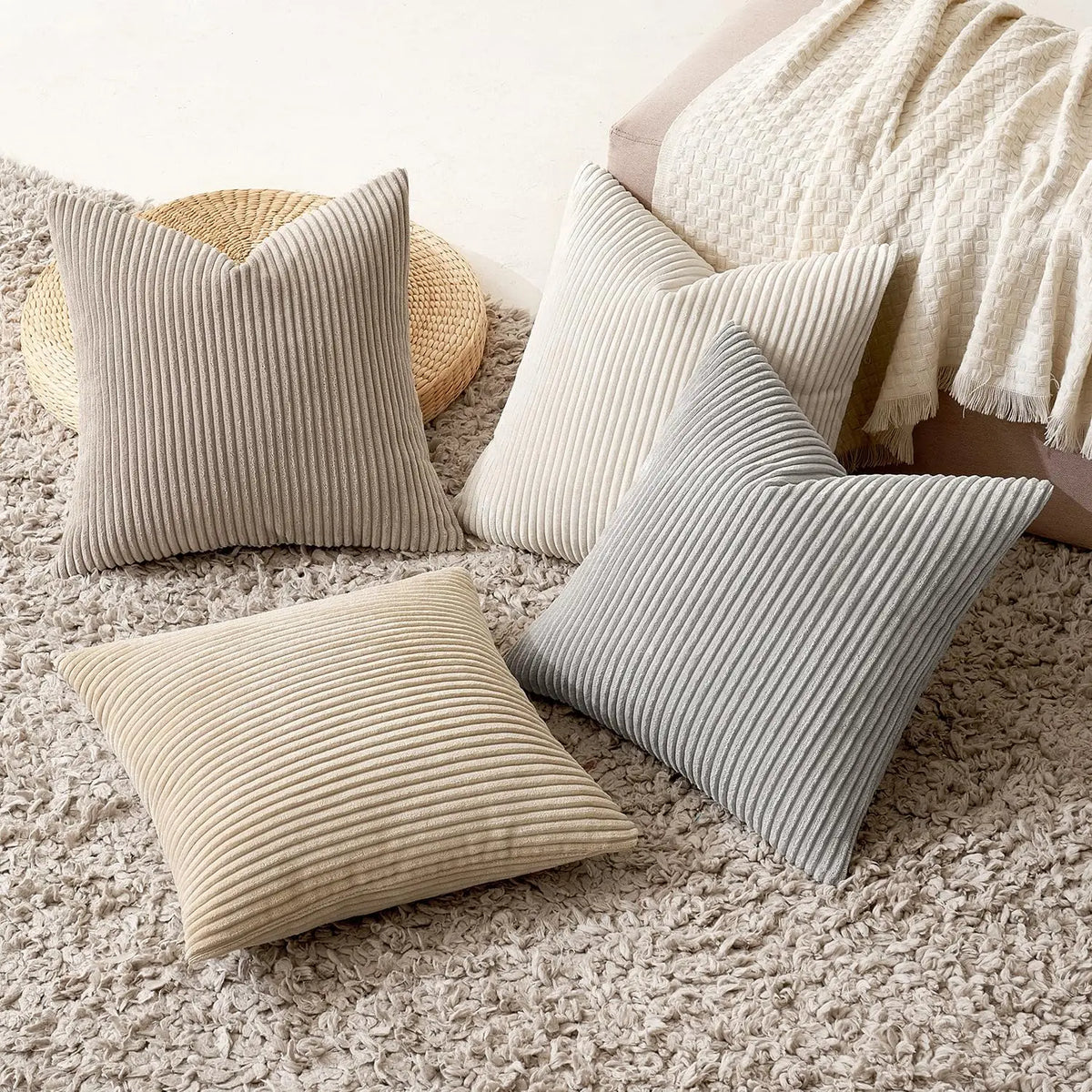 A collection of neutral-toned corduroy striped throw pillows resting on a beige textured rug.