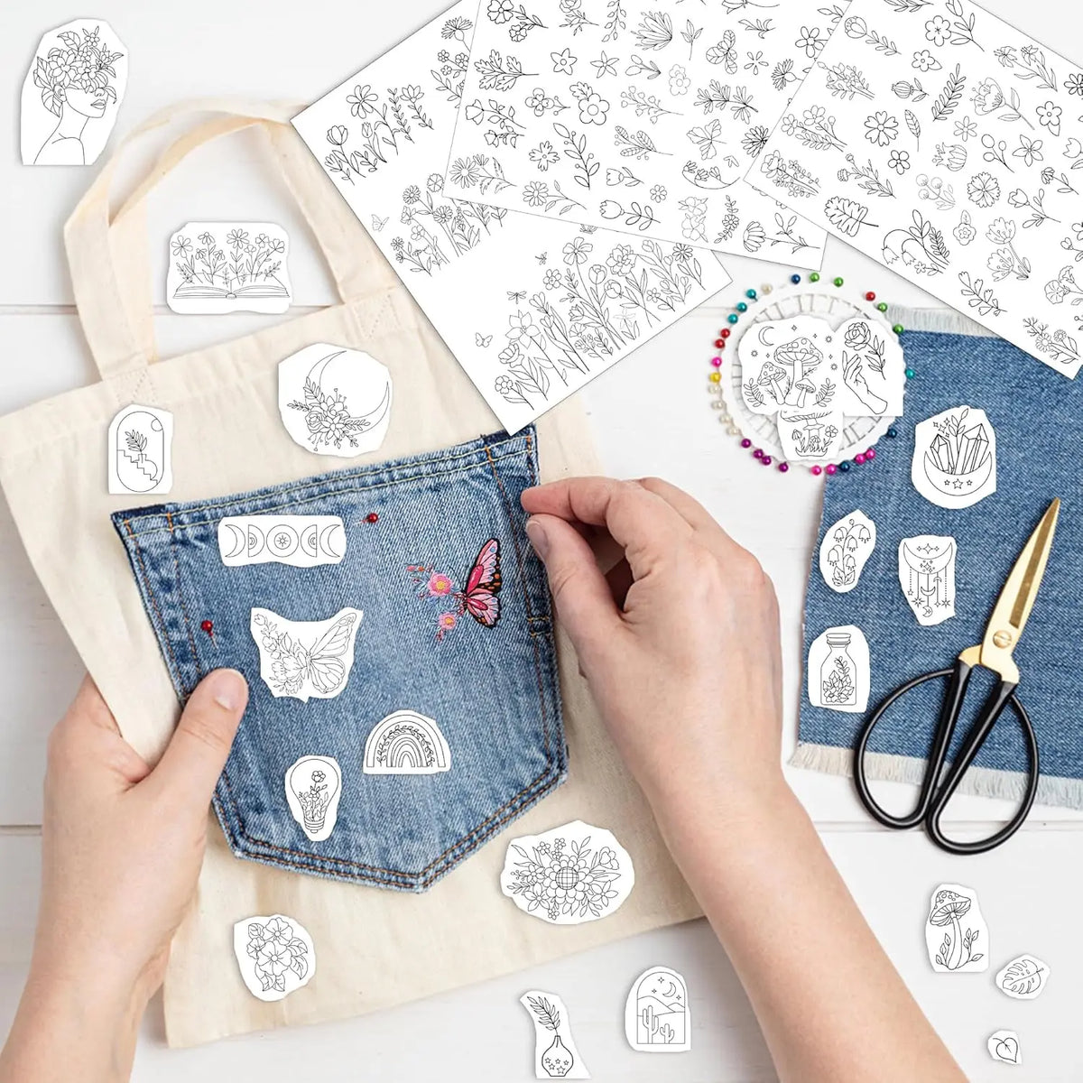 Hands are sewing a piece of denim fabric with white embroidery patterns and a yellow canvas bag in a bright studio setting.