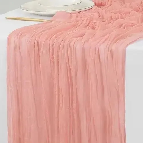 A flowing, dusty rose colored rustic gauze table runner draped elegantly on a white surface.