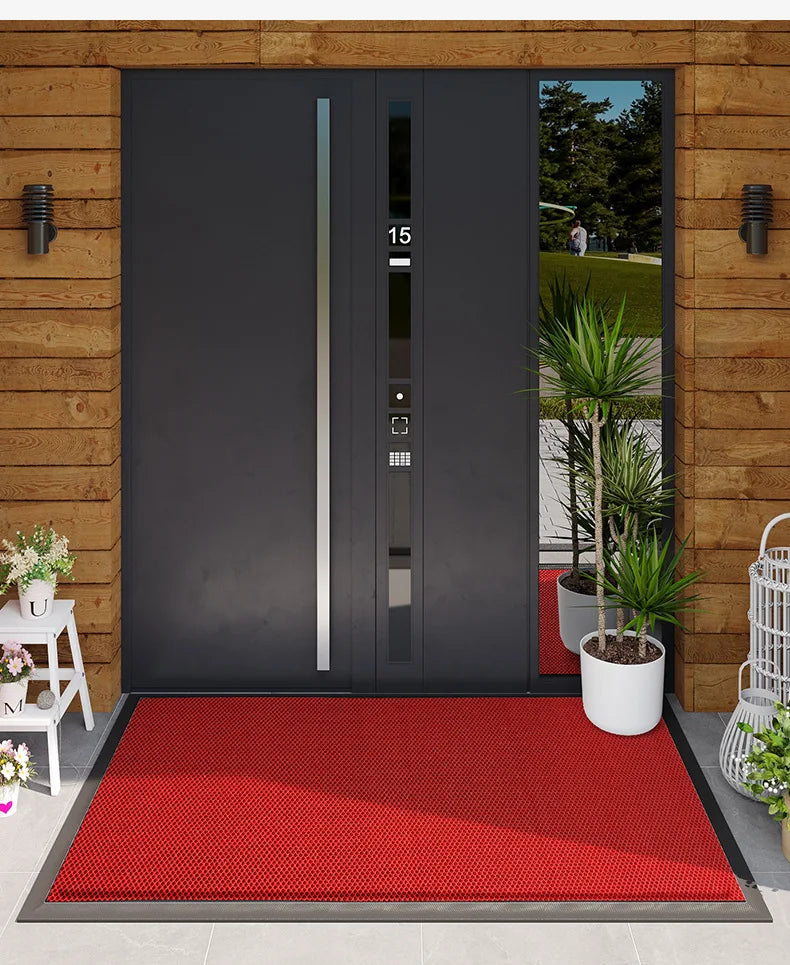 A modern dark gray double door with vertical silver accents set into a wooden wall, featuring a red doormat on the ground.
