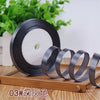 Roll of black satin ribbon with a white core displayed on a wooden board
