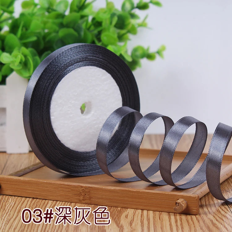 Roll of black satin ribbon with a white core displayed on a wooden board