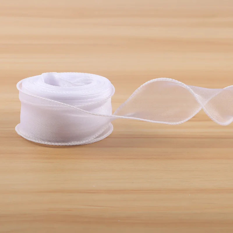 A roll of sheer white satin ribbon is unwinding on a wooden surface.
