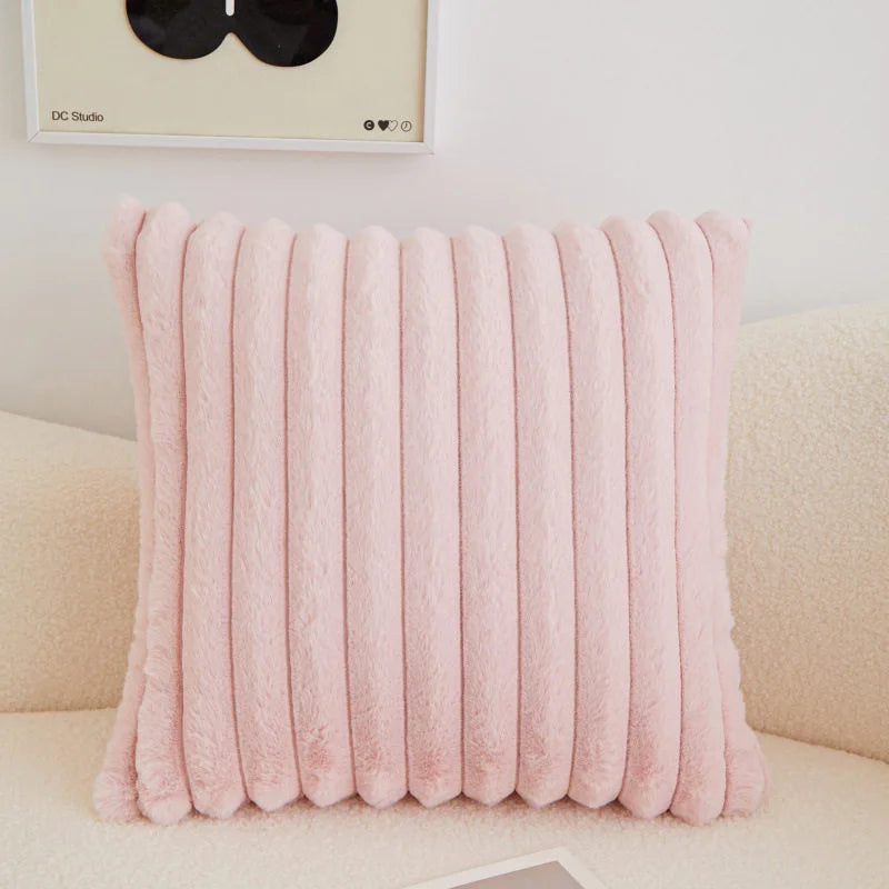 A pink plush winter throw pillow cover with vertical ribbed texture resting on a light-colored sofa.