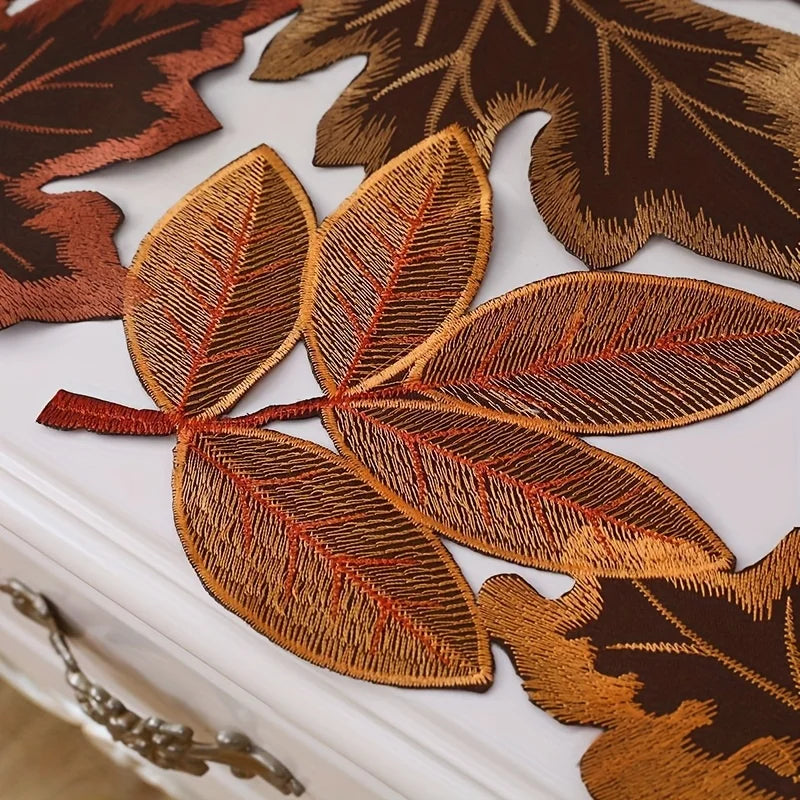 A decorative maple leaf table runner featuring various shades of brown and orange embroidery.