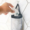 A hand is holding a white plastic bag dispenser rack with a black strap and a clear plastic container.