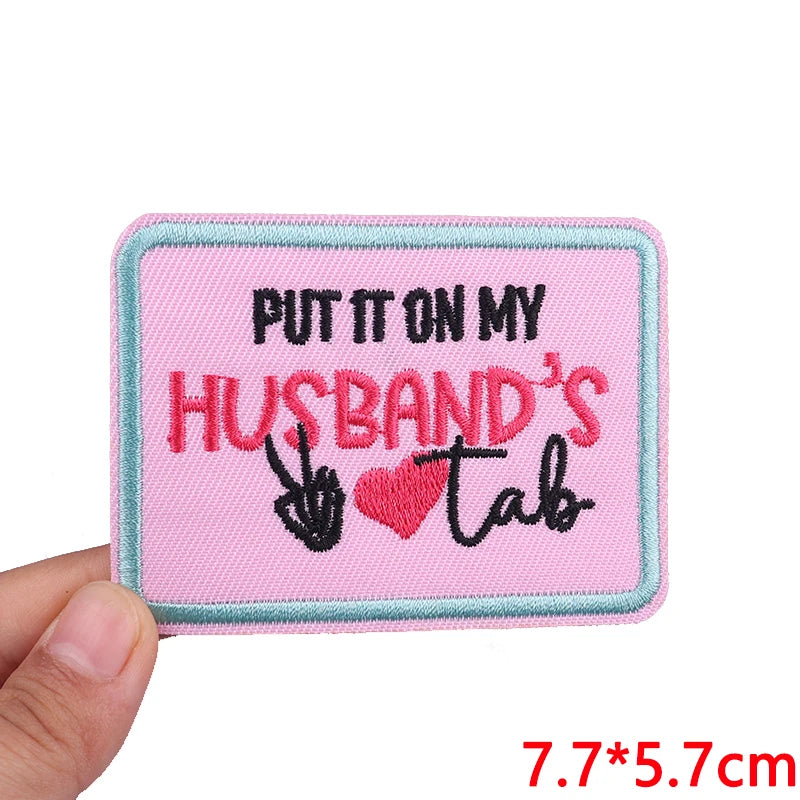 Pink embroidered patch with the text Put it on my husband's tab in black and pink thread
