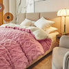 A pink quilted fleece blanket is spread over a beige bed with white pillows and modern decor.