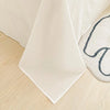 A white organic cotton flat sheet and pillowcase are folded on a light wooden surface.