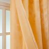 Flowing peach gold curtains with a feather jacquard pattern hanging in a bright room.