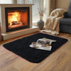 A plush solid black area rug placed on a wooden floor in a living room setting.