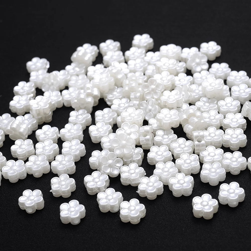 A pile of small white imitation pearl flower spacer beads for DIY jewelry.