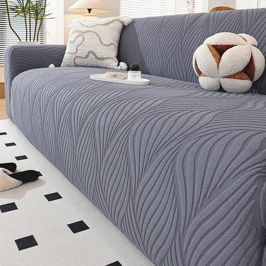 A gray stretch sofa cover featuring a vertical ribbed texture and an elastic edge, displayed on a sofa.