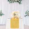 A white table with a golden sequin runner, floral centerpiece, and sheer white curtains.