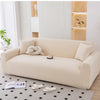 A beige stretchable elastic sofa cover with a light-colored sofa and decorative items in a bright room.