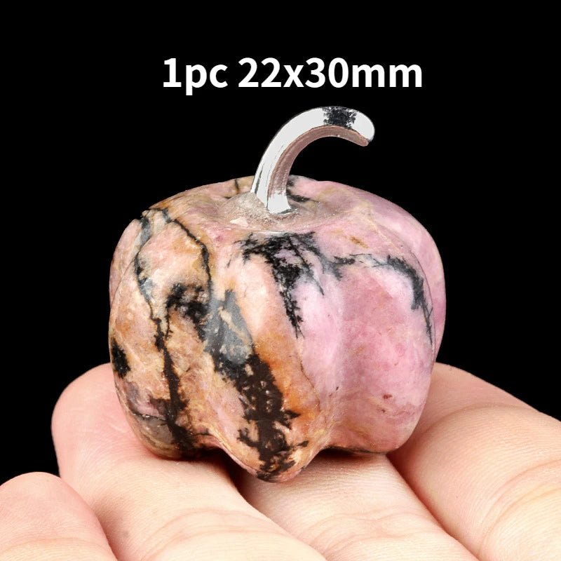 A pink and black marbled natural stone pumpkin figurine with a silver stem is held in a hand.