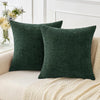 A solid dark green chenille throw pillow cover resting on a cream knitted blanket.