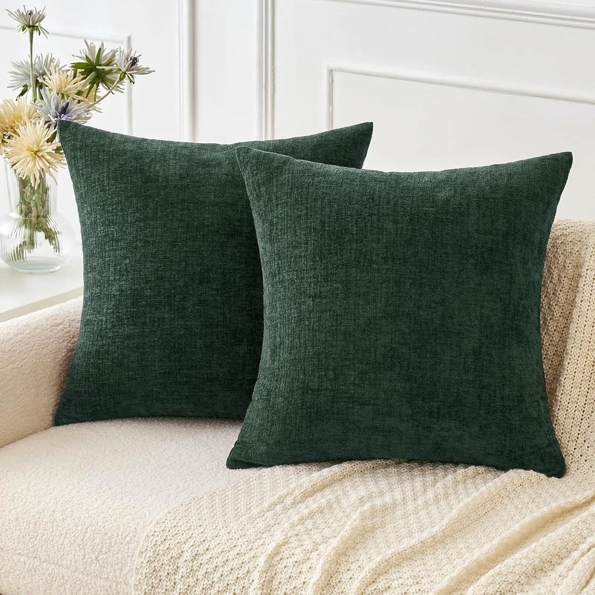 A solid dark green chenille throw pillow cover resting on a cream knitted blanket.