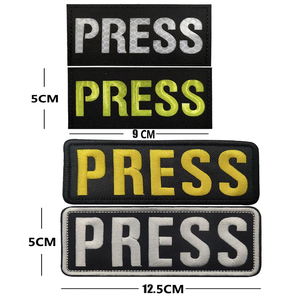 Four embroidered press patches in black, yellow, and white with hook and loop backing shown side by side.