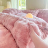 A hand is touching a fluffy pink rabbit fleece duvet cover on a bed.