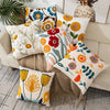 A collection of embroidered floral canvas throw pillows in shades of orange, yellow, green, and white on a neutral sofa.
