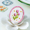 A pink and white cream-colored flower sticker is displayed on a white petal, surrounded by small floral stickers.