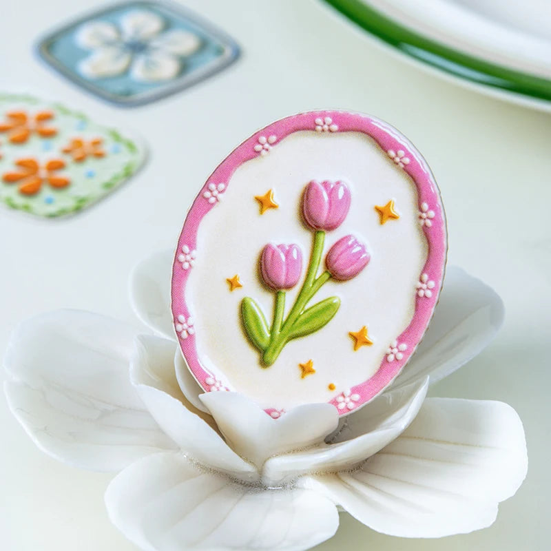 A pink and white cream-colored flower sticker is displayed on a white petal, surrounded by small floral stickers.