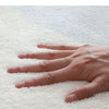 A hand is gently touching a fluffy white rug or textile surface.