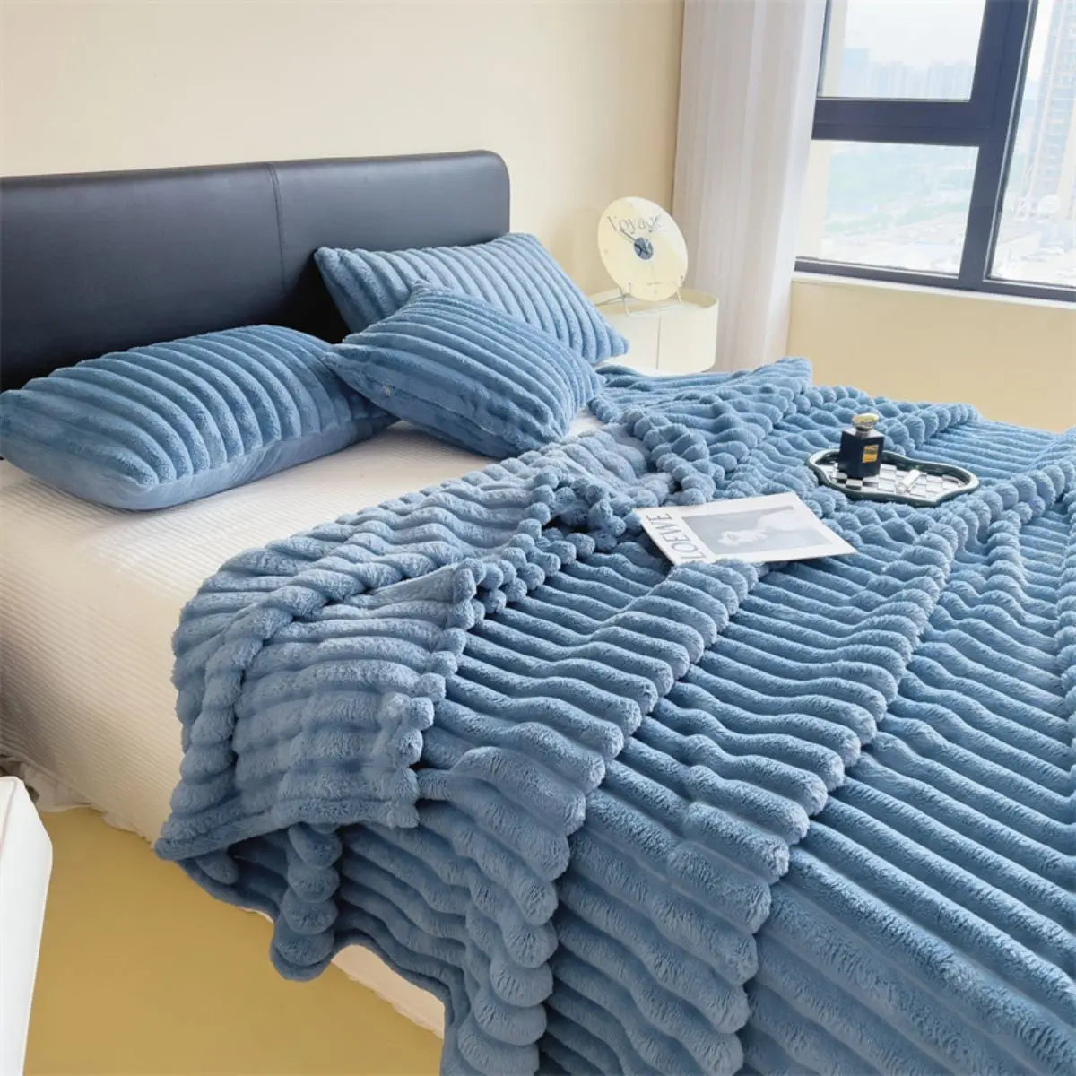 A thick blue striped cozy blanket is draped over a bed, next to a window.