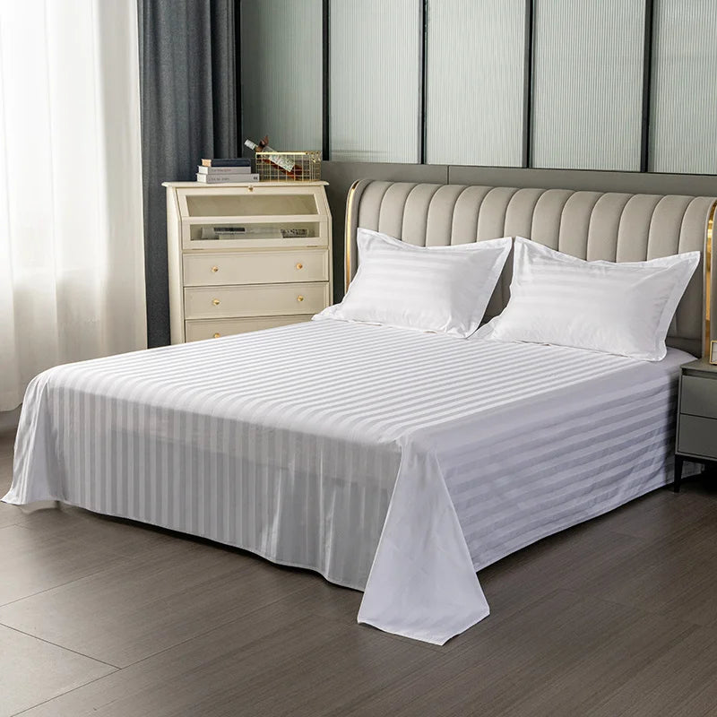 A bed dressed with white and gray striped cotton flat sheet bedding against a modern upholstered headboard.