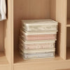 Stack of clear mesh storage bags filled with folded bed sheets and blankets inside a wooden cabinet
