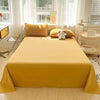 A bright yellow organic cotton bedding set featuring a flat sheet, pillows, and a small stuffed animal on a bed.