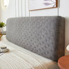 A gray plush quilted headboard cover resting on a white bed with a cream textured blanket.