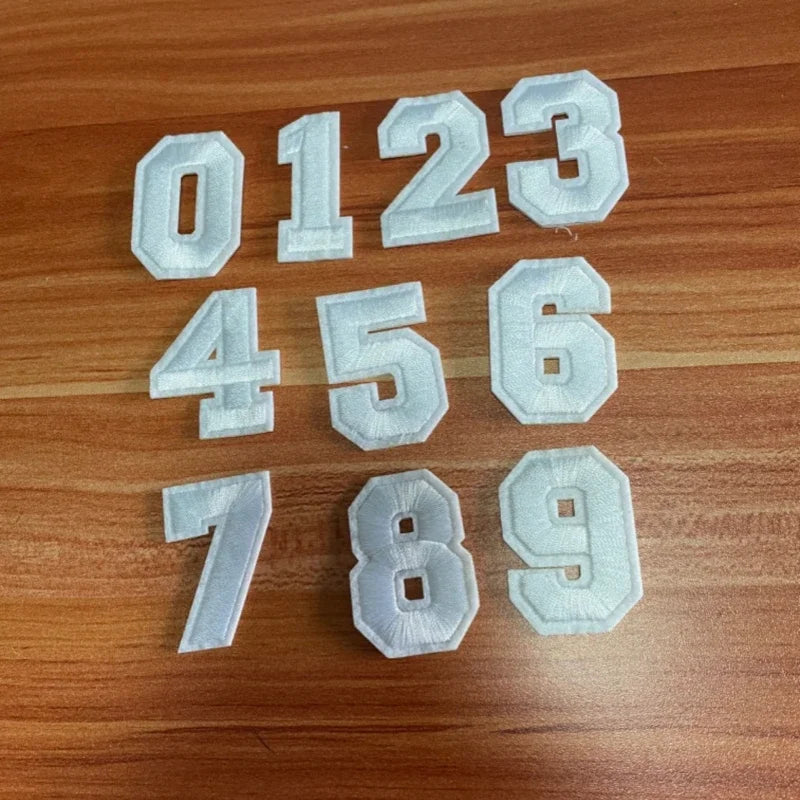 A set of white, customizable number patches (0 through 9) laid out on a wooden surface.
