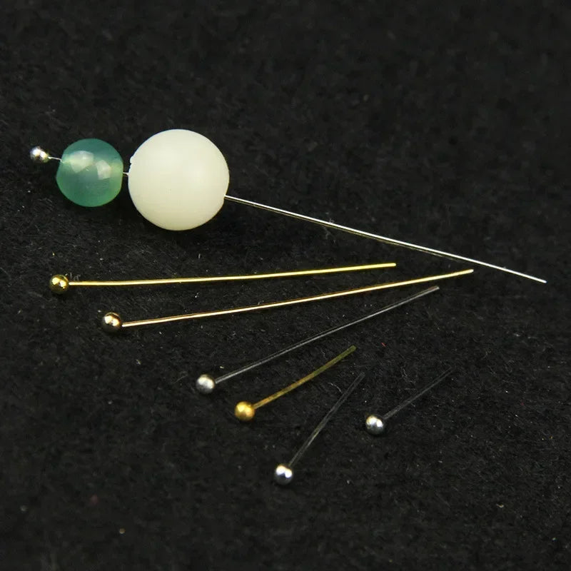 A collection of stainless steel ball head pins in various sizes and finishes, including green and white beads.