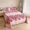Pink flat bed sheets with a red floral print displayed on a bed in a bright room.